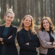 Der Vorstand des Kunstvereins Haan: Drei Frauen stehen lächelnd mit verschränkten Armen nebeneinander in einem sonnendurchfluteten Wald. Patrycja Karle, Pia Stojkovic und Frauke Wagener präsentieren sich als neues Leitungsteam – selbstbewusst, offen und nahbar.